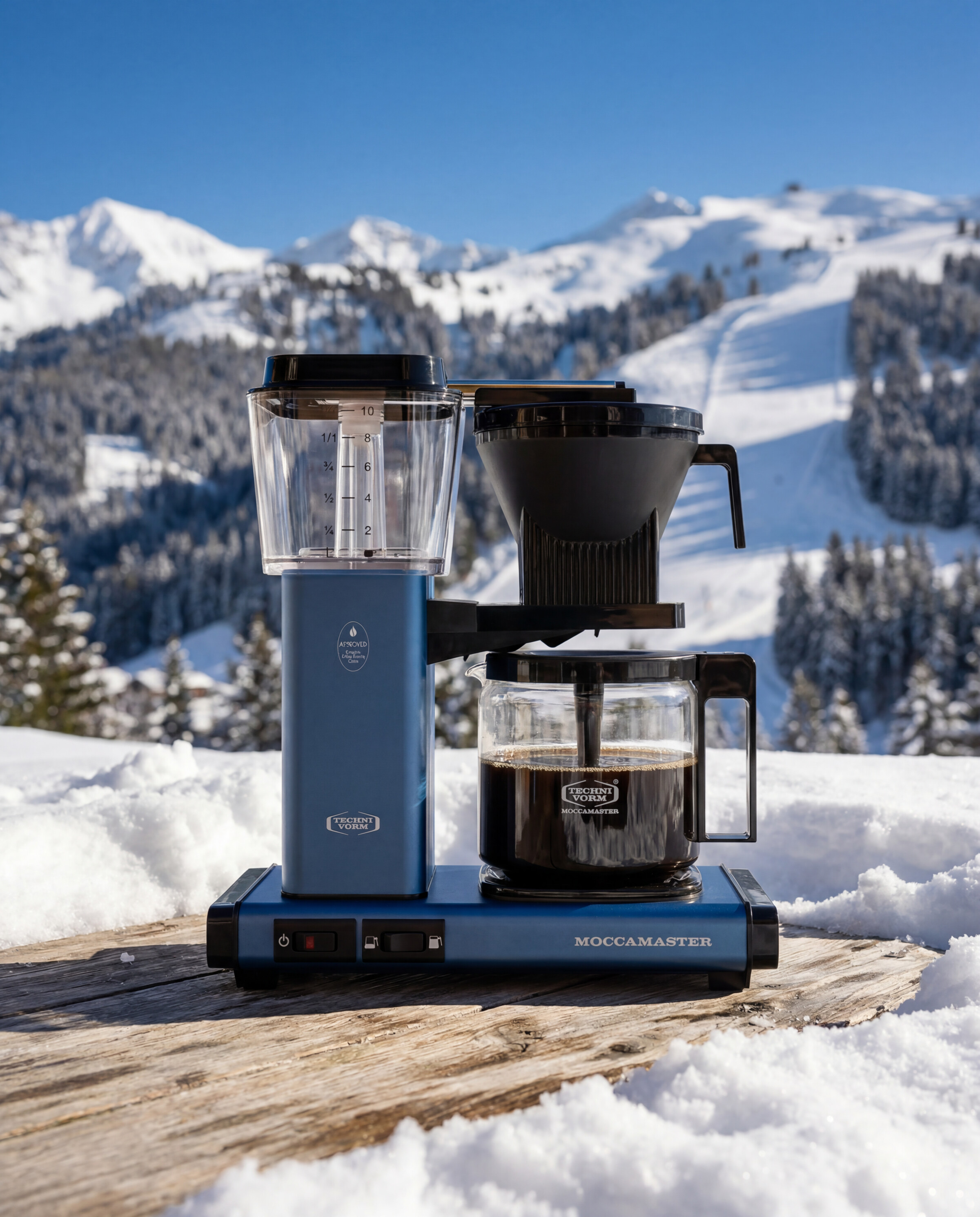 Moccamaster product still - Blue brewer on a timber deck above alpine chalets